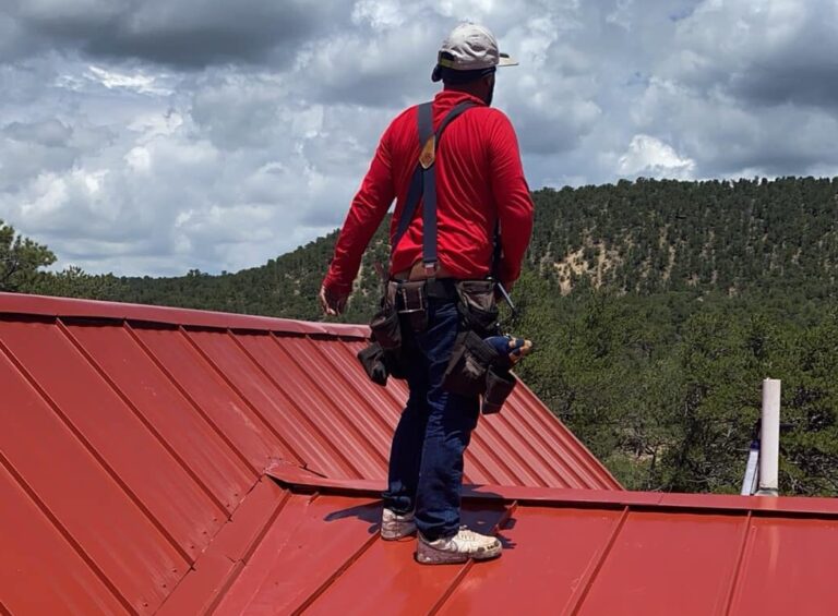 Roofer inspecting a red metal roof for storm damage in Southern Colorado