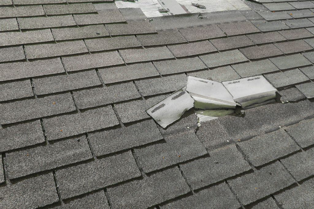 Broken asphalt roof shingles on a residential roof showing storm or impact damage in Pueblo Colorado.